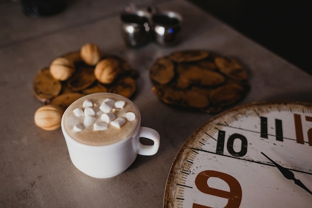 Taza de café con malvaviscos sobre un fondo de relojes