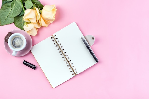 La taza de café de la mañana para el desayuno, el cuaderno vacío, el lápiz y se levantó en la vista superior rosada de la tabla