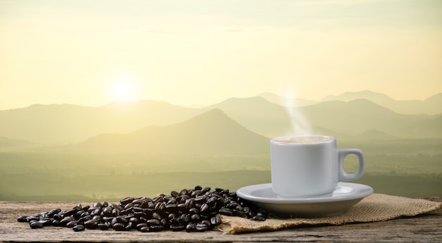 Taza de café de la mañana y granos de café tostado con sol de montaña