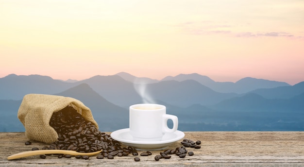 Taza de café de la mañana y granos de café tostado con sol de montaña