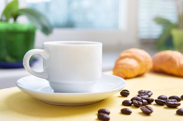 Una taza de café por la mañana en la mesa frente a la ventana y croissants recién hechos para el desayuno.