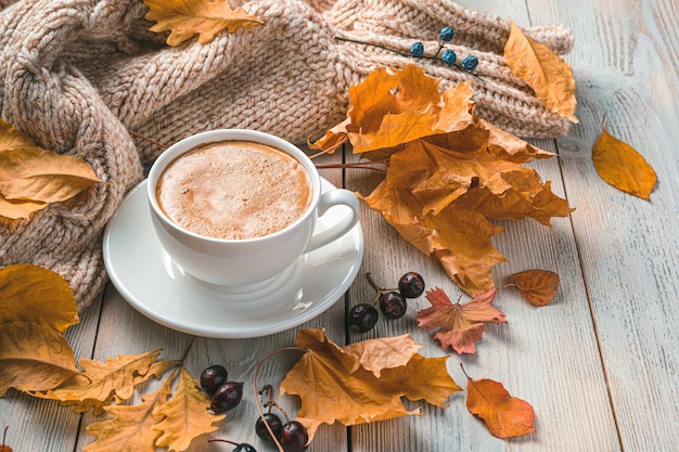 Una taza de café en una mañana de otoño con el telón de fondo de follaje y un suéter