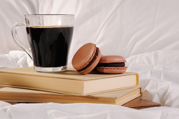 Taza de café por la mañana con pasteles de chocolate Macarrones, sobre una pila de libros en la cama.