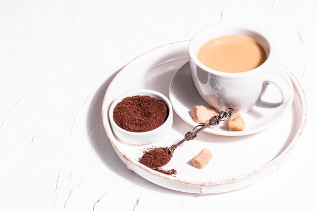 Taza de café por la mañana. Polvo molido, azúcar morena, reposar. Buen humor, fondo de yeso blanco, lugar para el texto