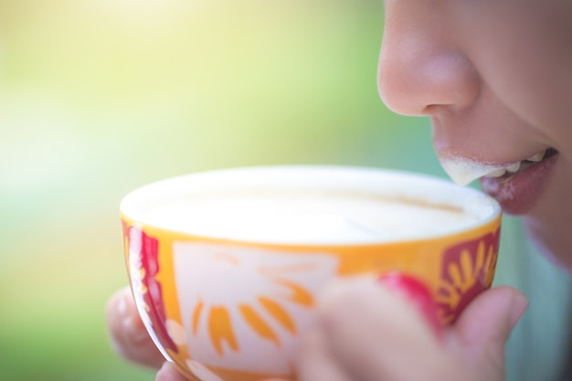 Una taza de café en la mano de una mujer que sorbe el café en un fondo natural.