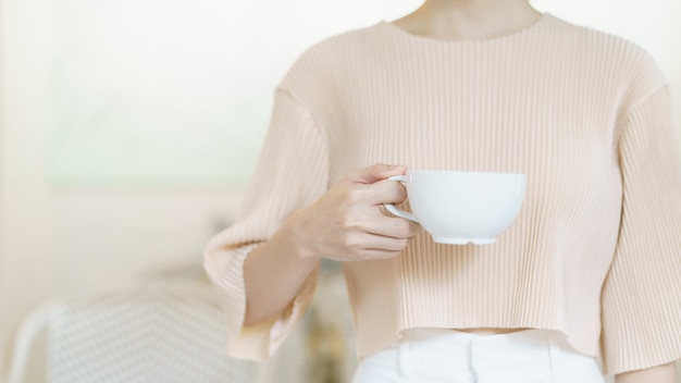 Taza de cafe. Mano de mujer con té o café. Blanco taza de bebida caliente en la mañana.