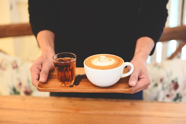 Taza de café en la mano sobre la mesa de madera en la cafetería con fondo de granos de café, café servido.