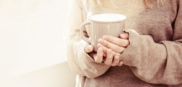 Taza de café en manos femeninas con suéter de punto