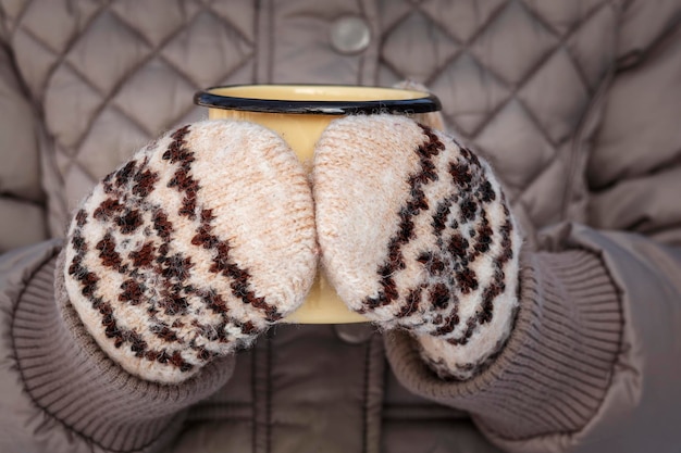 Taza de café en manos con guantes de lana étnicos Manos femeninas sosteniendo una taza de café en guantes tejidos