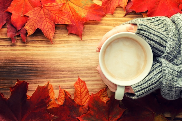 Una taza de café en las manos en un taburete de madera contra el fondo