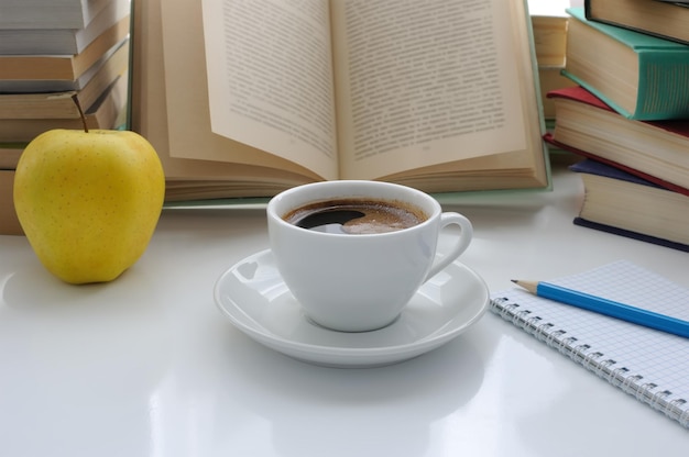 Una taza de café y una manzana en una mesa entre libros.