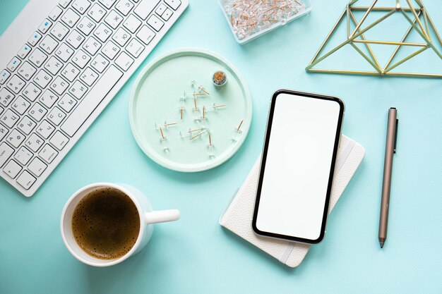 Taza de café y maqueta de teléfono inteligente en el lugar de trabajo azul pastel de Lady freelancer en la mesa