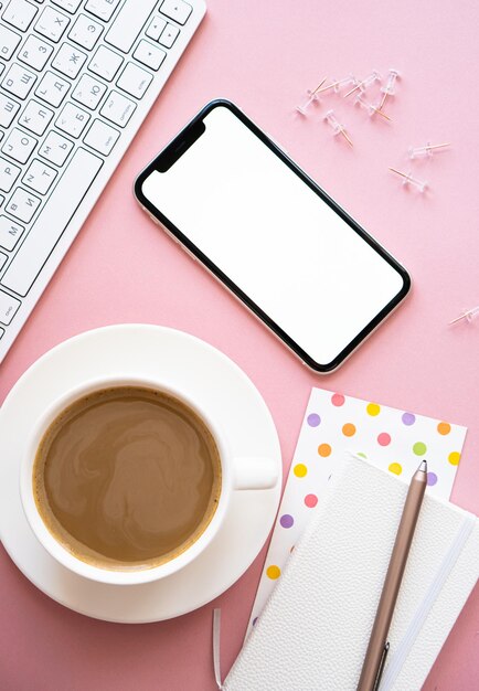 Taza de café y maqueta de teléfono inteligente en el lugar de trabajo rosa pastel de Lady freelancer's home