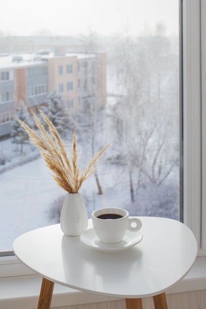 Taza de café en la mesa blanca junto a la ventana en invierno