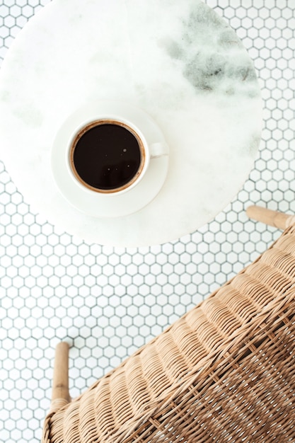 Taza de café en la mesa de café de mármol en mosaico blanco con silla de ratán