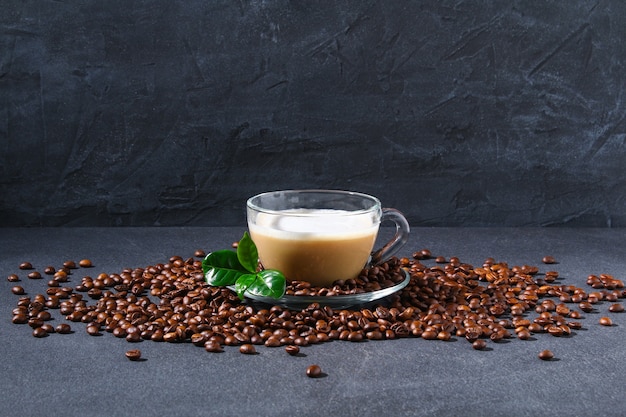 Taza de café en una mesa gris con granos de café y hojas de café