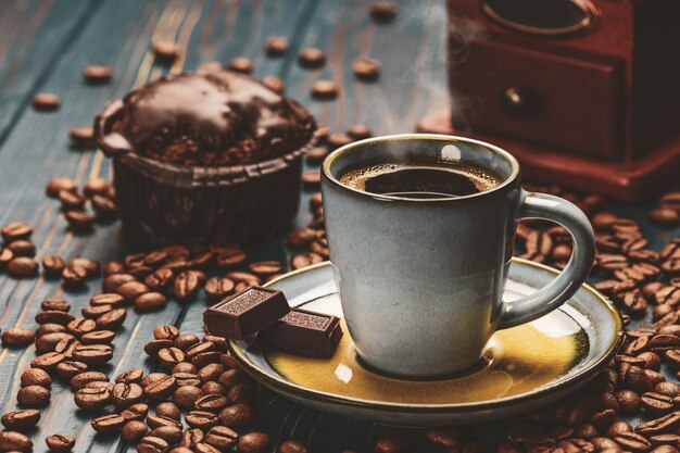 Taza de café en una mesa de madera azul con granos de café y chocolate.