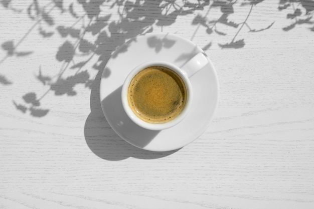 Taza de café en la mesa de madera blanca y sombras de la planta Mañana de verano café desayuno sombra ligera