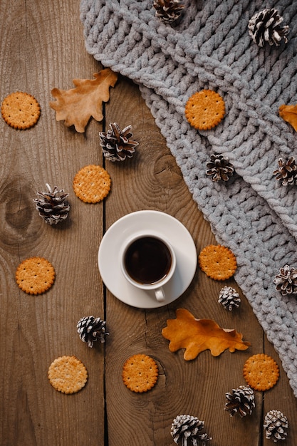 Una taza de café en una mesa de madera con galletas, hojas y conos