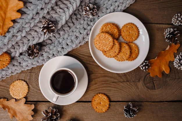 Una taza de café en una mesa de madera con galletas, hojas y conos