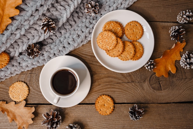 Una taza de café en una mesa de madera con galletas, hojas y conos