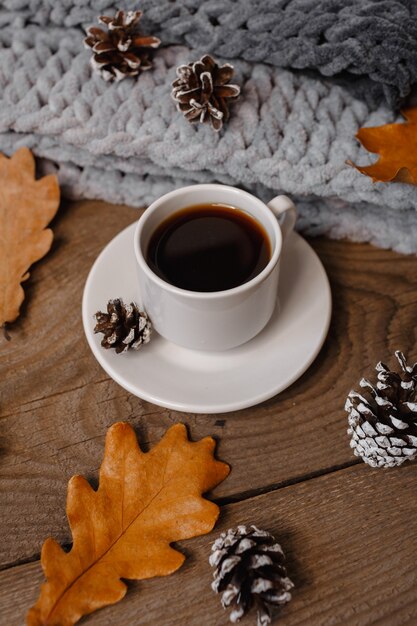 Una taza de café en una mesa de madera con galletas, hojas y conos