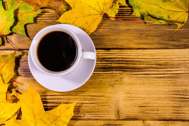 Taza de café y montón de hojas de arce amarillas en una mesa de madera Vista superior