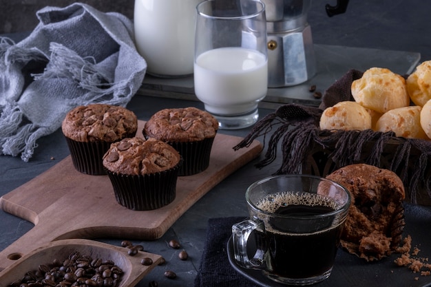 Una taza de café, muffins de chocolate, panes de queso y leche.