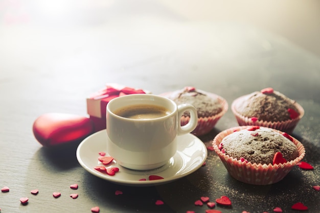 Taza de café, muffins de chocolate y regalo. Luz solar, enfoque selectivo, vintage. El concepto de una mañana romántica, cumpleaños o día de san valentín.