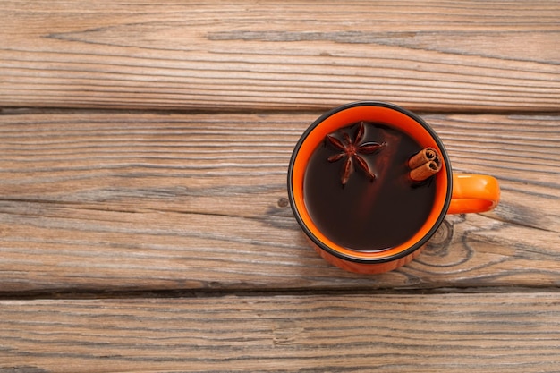 Taza de café naranja con especias sobre fondo de madera