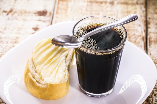 Taza de café negra y dulce con cuchara de metal, bebida caliente típica de Brasil, servida en panaderías