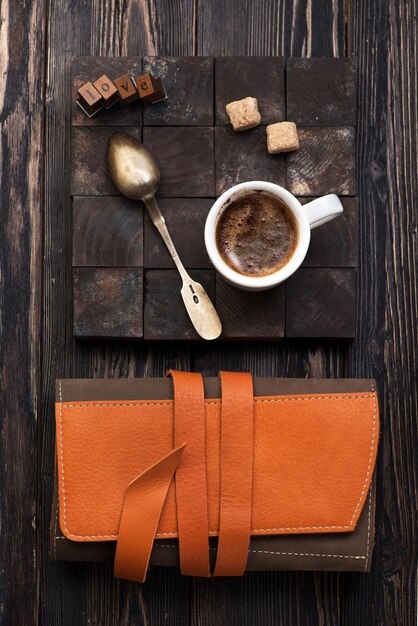 Taza de café negro con azúcar sobre un fondo de madera, estuche de cuero y texto de amor, plano