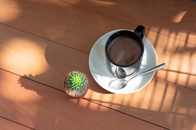 Taza de café negro y cactus en luz de madera