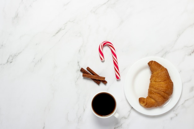 Taza con café negro, croissant, bastón de caramelo sobre un fondo de mármol