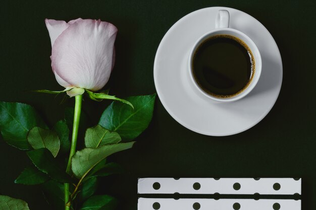 Taza de café negro, cuaderno y rosa rosa sobre negro, vista superior, espacio de copia. Tonificado