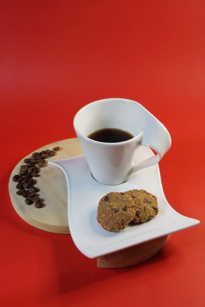 Una taza de café negro y dos galletas de chocolate con un fondo rojo brillante