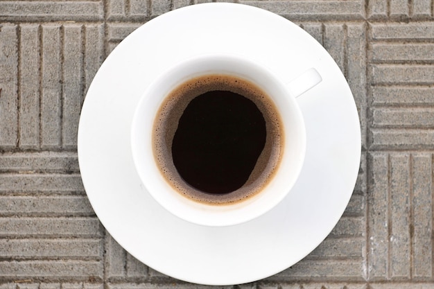 Una taza de café negro fragante se encuentra sobre una baldosa de hormigón Vista superior