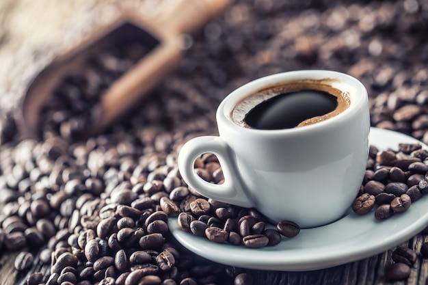 Taza de café negro con frijoles en la mesa de madera.