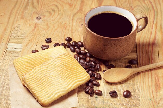 Taza de café negro y galletas dulces en la mesa de madera antigua