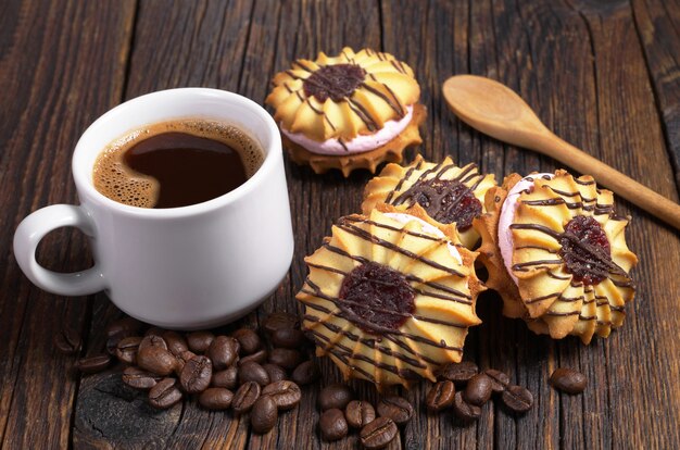 Taza de café negro y galletas de mantequilla con crema y chocolate en la mesa de madera