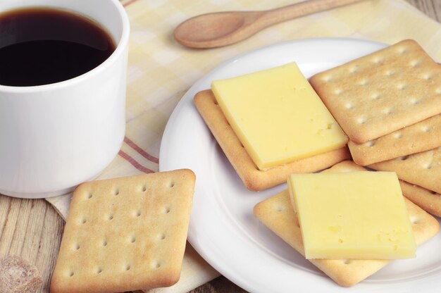 Taza de café negro y galletas saladas con queso y sobre mesa de madera