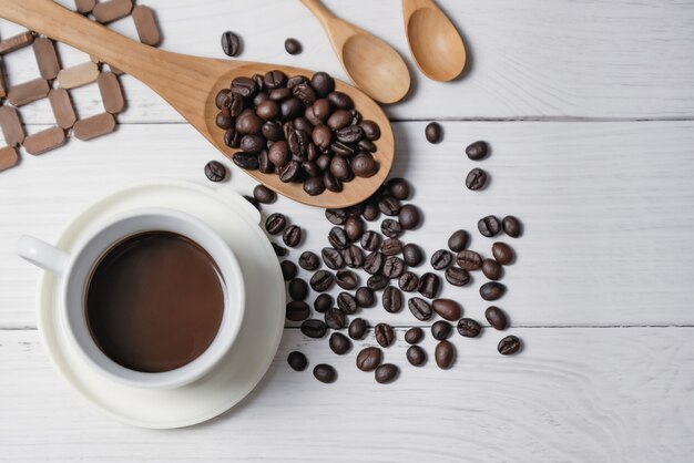 Taza de café negro y granos de café buenos elementos esenciales en la mesa de madera blanca. Vista superior.