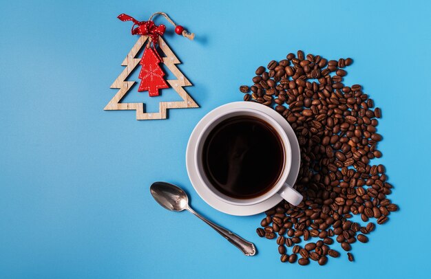 Taza de café negro y granos de café sobre fondo azul, copie el espacio para el texto. Concepto de navidad.