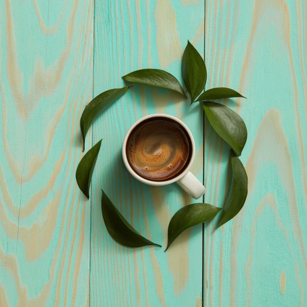 Taza de café negro y hojas verdes. Endecha plana