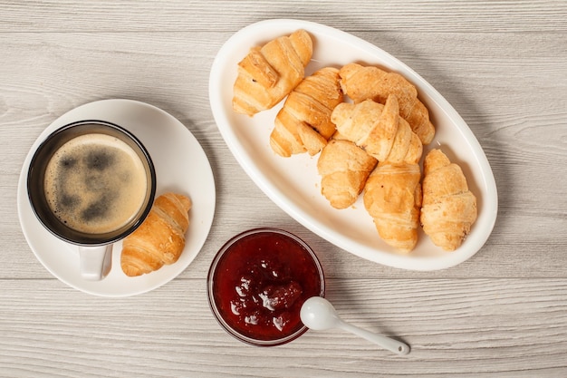 Taza de café negro con platillo croissants recién hechos en plato de porcelana blanca