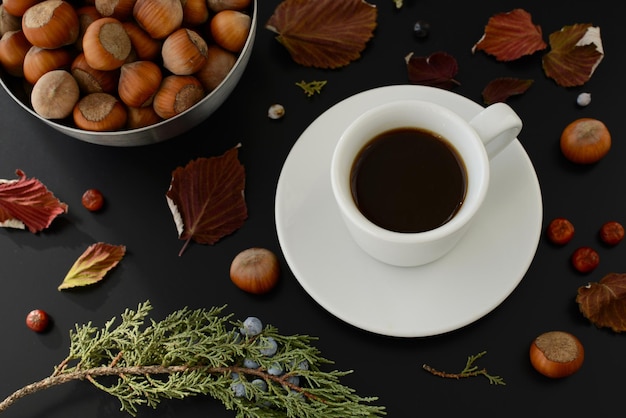 Taza de café negro plato avellanas rama de enebro y hojas caídas de otoño sobre un fondo de mesa negro