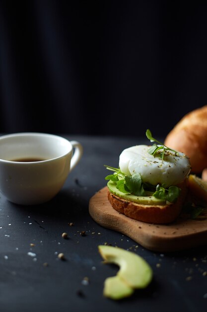 Taza de café negro y sándwich con aguacate y semillas de huevo escalfado y microgreen Superficie negra Espacio de copia Desayuno saludable