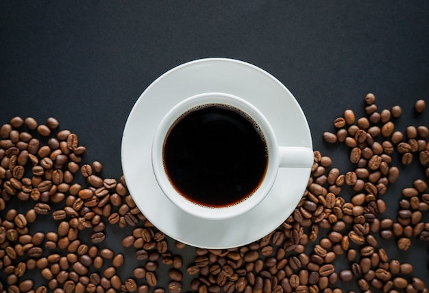 Taza de café negro sobre fondo negro con granos de café tostados