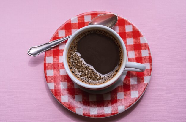 Una taza de café negro sobre fondo rosa.