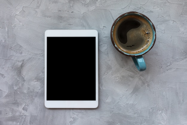 Taza de café negro y tableta sobre fondo gris rústico. Plano, vista superior, espacio de copia, plantilla de redes sociales, concepto de mañana e internet